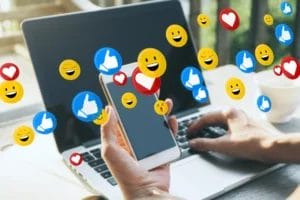 Person using a smartphone and laptop with social media reaction icons, representing digital marketing and Singapore social media agency services for modern brands.