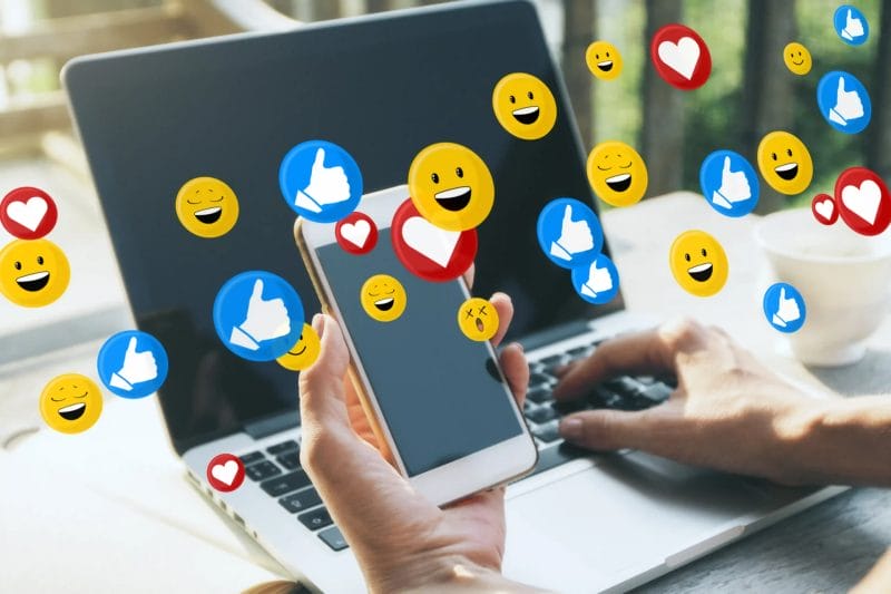Person using a smartphone and laptop with social media reaction icons, representing digital marketing and Singapore social media agency services for modern brands.